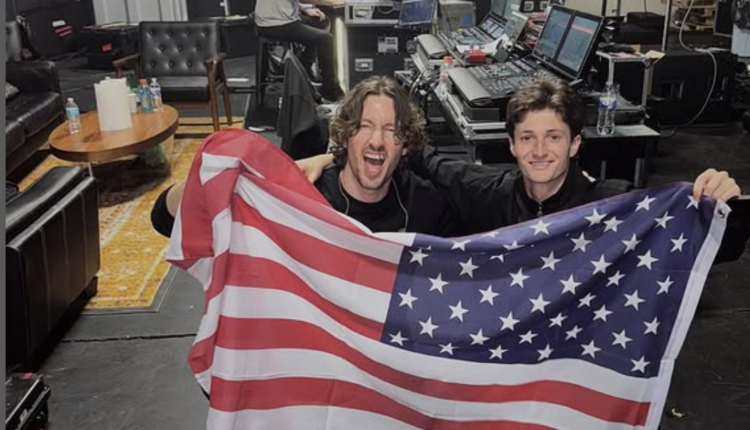 Two men holding an American flag in the backstage of a concert venue